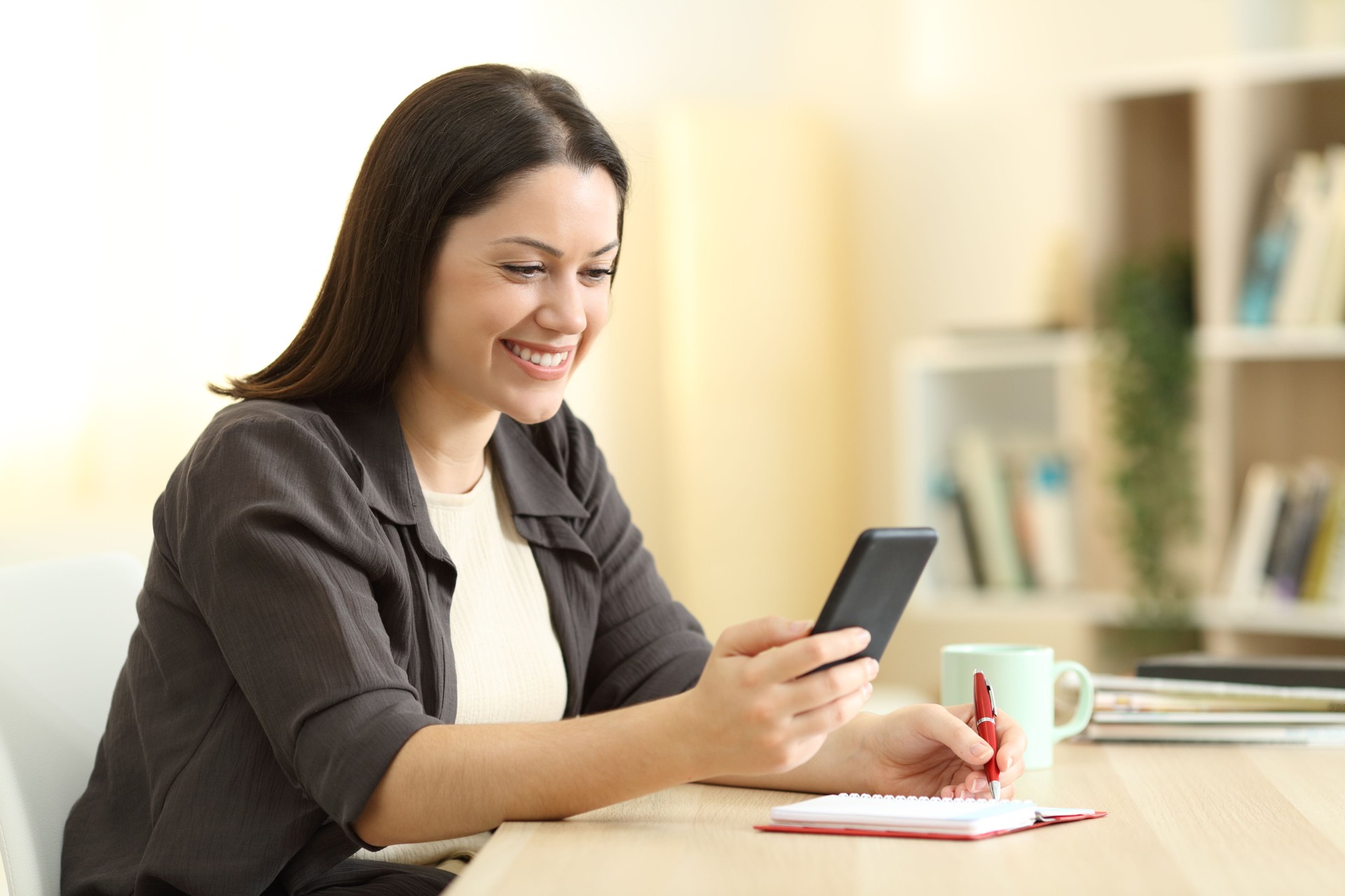 Happy woman writing in agenda and checking phone